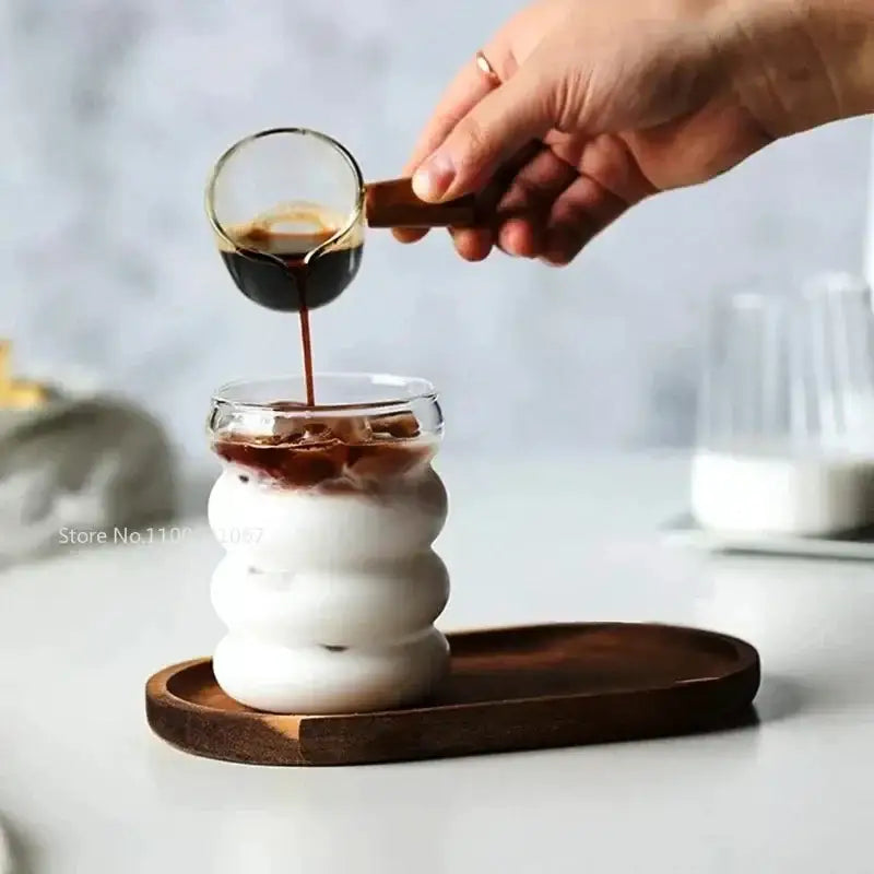 A clear glass coffee scoop with dark wooden handle pouring espresso into a white ribbed glass from decorbites glass cocktail cups set