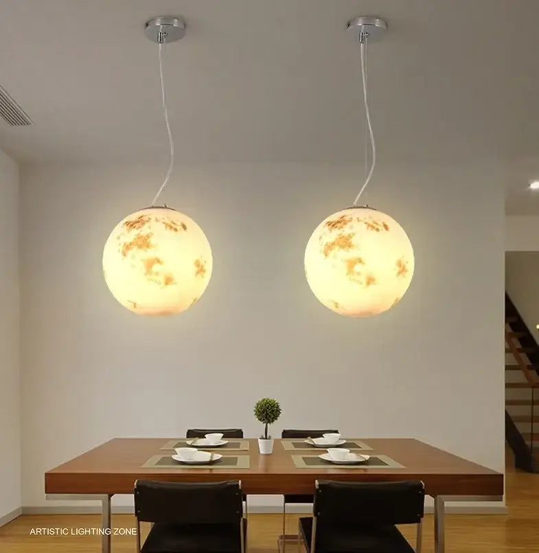 Two warm glowing nordic retro ball moon chandelier pendant lights with detailed crater surface for dining room use