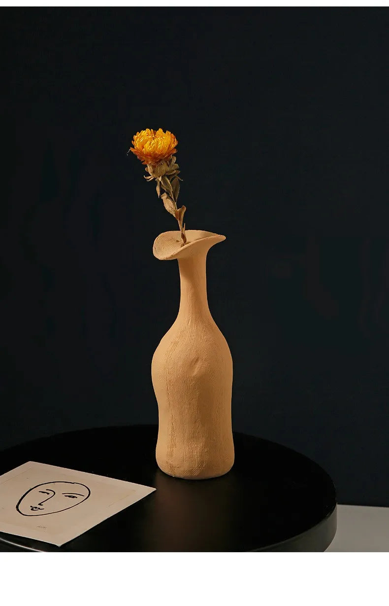 A beige ceramic nordic style modern vase with a smooth textured surface holding a dried yellow flower for home decoration
