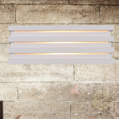 Modern white nordic style louvered wall sconce with warm light glowing through horizontal slats for bedroom use