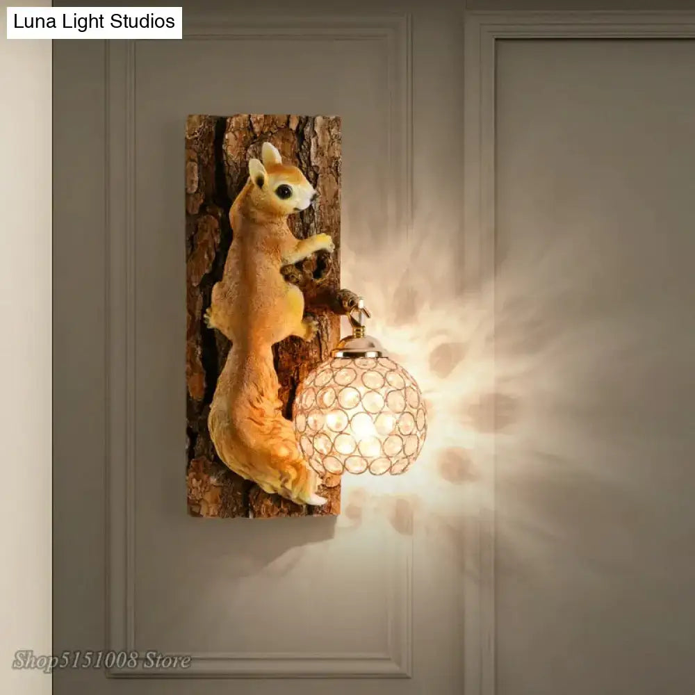 A nordic vintage style golden-brown resin squirrel wall lamp holding a crystal globe with brass finish on tree trunk base