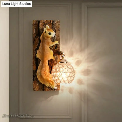 A nordic vintage style golden-brown resin squirrel wall lamp holding a crystal globe with brass finish on tree trunk base