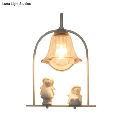 Warm-toned bell-shaped glass lamp with metallic frame and white arched frame casting light on ceramic figurines