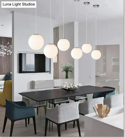Six nordic white glass ball pendant lights with frosted finish hanging in a modern dining room setting