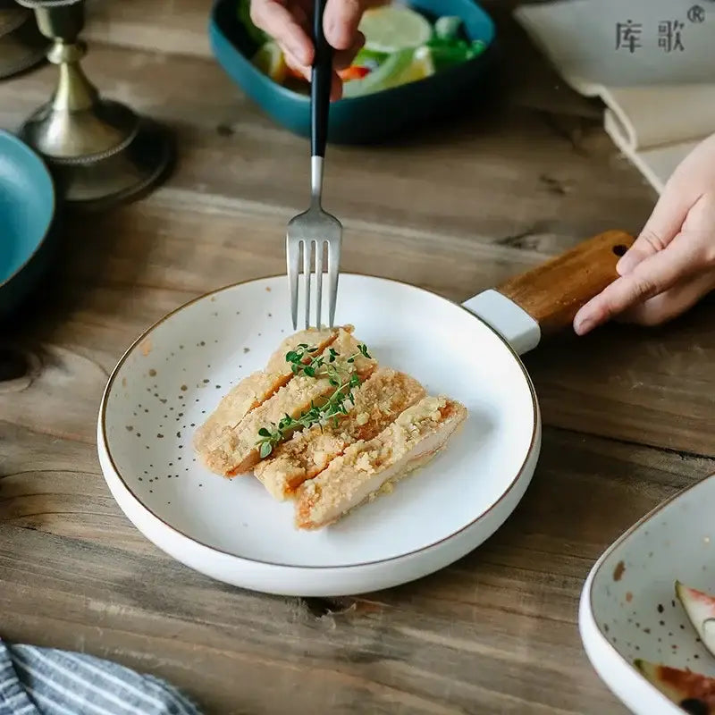 Nordic white speckled ceramic wood handle bowl with gold rim holding sliced fried chicken garnished with fresh herbs