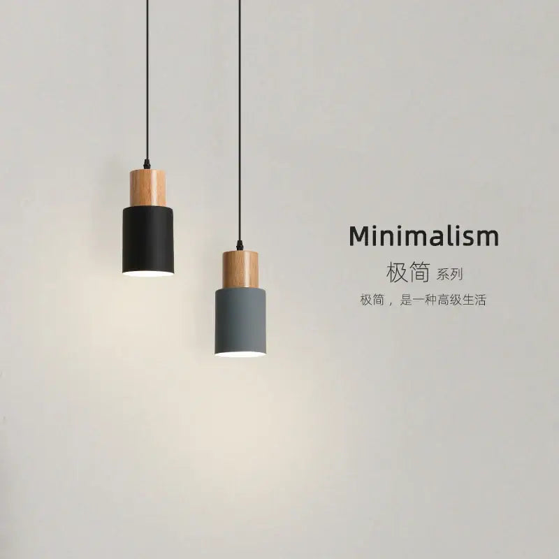 Two minimalist pendant lights with cylindrical matte black and gray shades and solid wood accents for kitchen or dining room