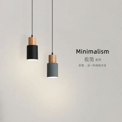 Two minimalist pendant lights with cylindrical matte black and gray shades and solid wood accents for kitchen or dining room