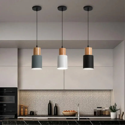 Three modern pendant lights with cylindrical gray white and black shades and solid wood top caps for kitchen or dining room