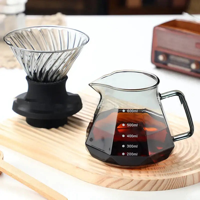 Octagonal clear decorbites glass coffee kettle with black measurement markings filled with dark liquid for brewing