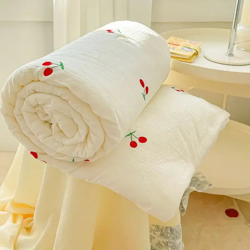 A soft off-white double layer yarn summer quilt with delicate red cherry embroidery rolled on a chair