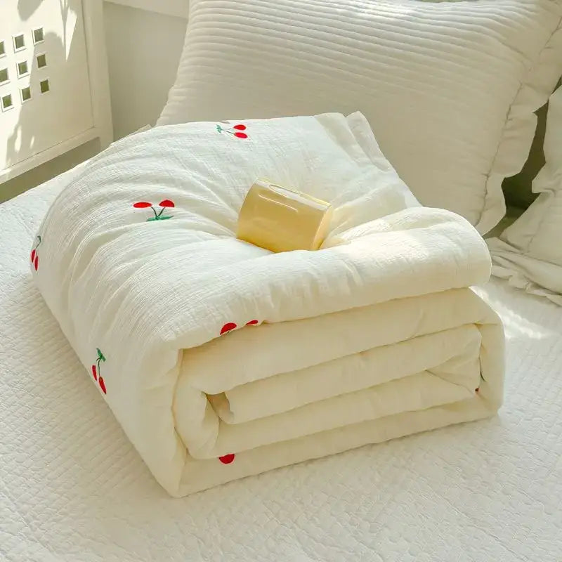 Off-white cherry embroidered double layer yarn summer quilt folded on bed showcasing its soft quilted texture
