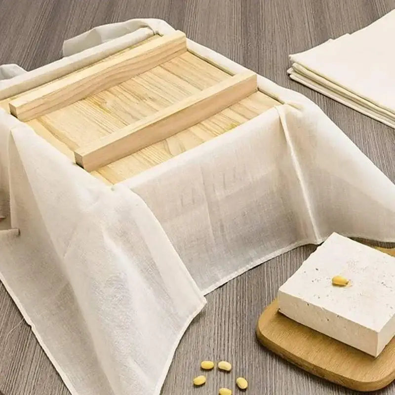 A light-colored wooden tofu press with a slatted lid wrapped in an off-white decorbites cotton tofu maker cloth