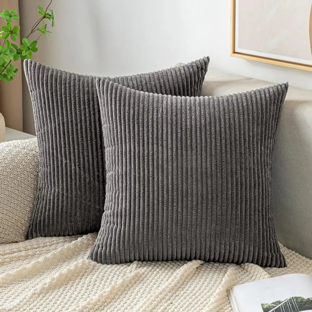 Two dark gray corduroy striped throw pillow covers with ribbed texture resting on off white knitted decorbites corduroy striped blanket