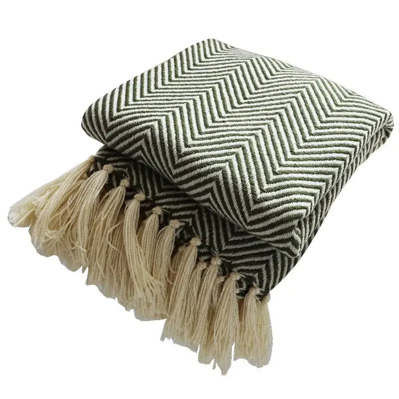 Folded decorbites geometric knitted blanket in olive green and cream with bold zigzag pattern and natural tassels