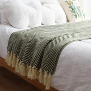 A soft olive green and cream decorbites geometric knitted blanket with herringbone pattern and fringed tassels for living room