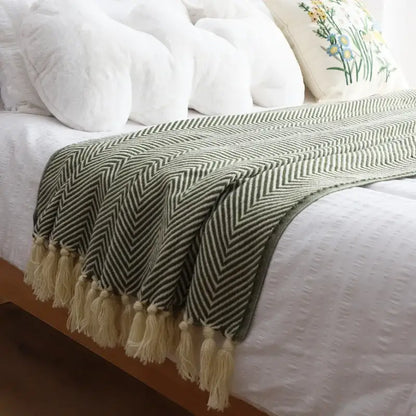 A soft olive green and cream decorbites geometric knitted blanket with herringbone pattern and fringed tassels for living room