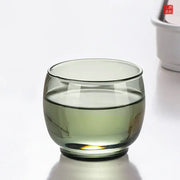 A translucent olive green decorbites glass tea cup with rounded base and smooth rim in a kung fu tea cup set