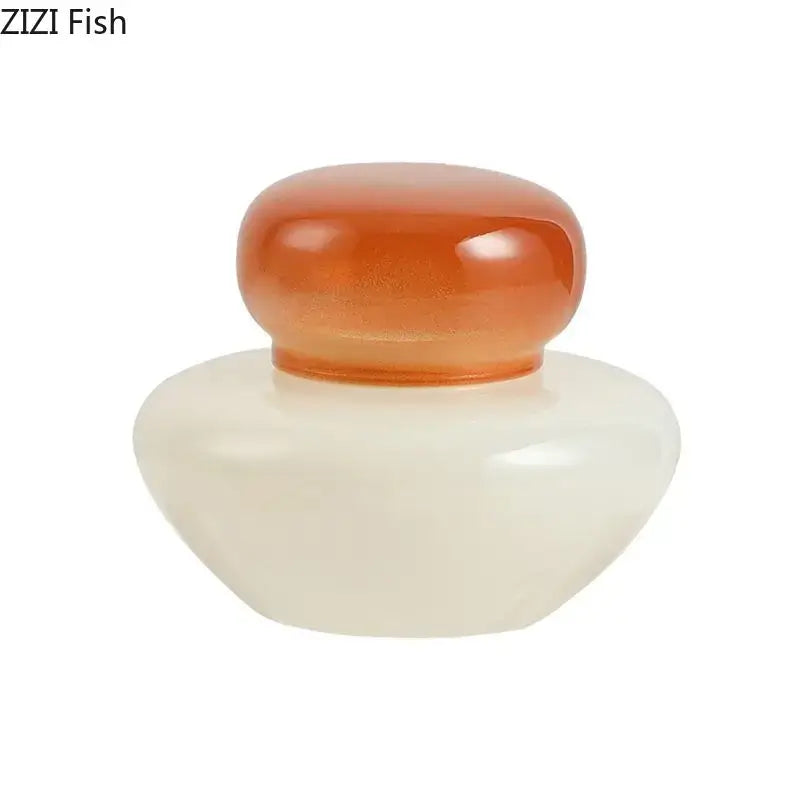 A smooth translucent orange glass lid on a rounded white ceramic base of a glass storage jar for kitchen candy