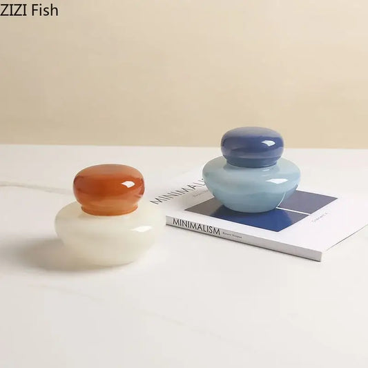 Two glossy orange and blue glass storage jars with rounded translucent bodies and matching domed lids for kitchen use