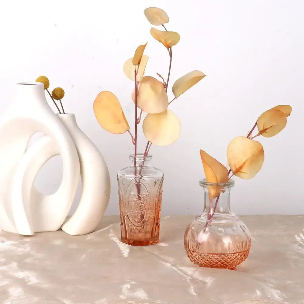 A clear glass bud vase with embossed floral design and gradient orange glass tint holding dried yellow leaves