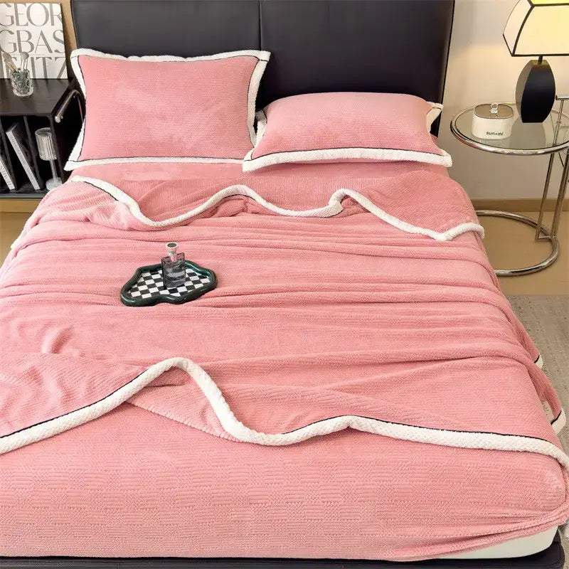 Pink plush blanket with white fleece trim and wavy edge shown with orange and gray decorbites carved velvet blanket throw