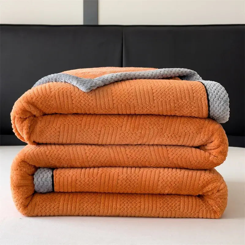 Stacked orange fleece blanket with gray textured trim from decorbites carved velvet blanket collection for living room use