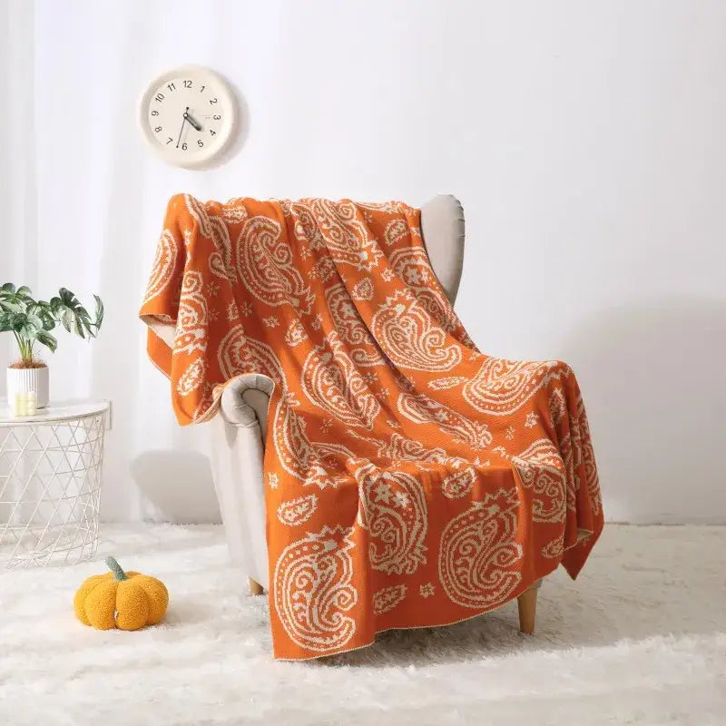 Orange paisley-patterned throw blanket with cream accents draped on chair featuring decorbites cashew pattern