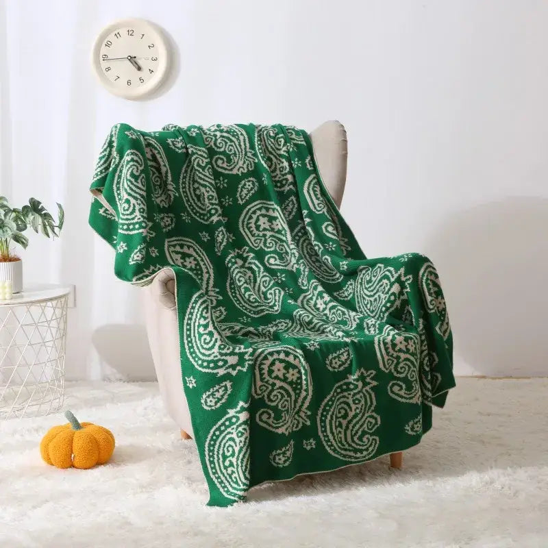 Green and white knit throw blanket with decorbites cashew pattern draped over chair for living room use