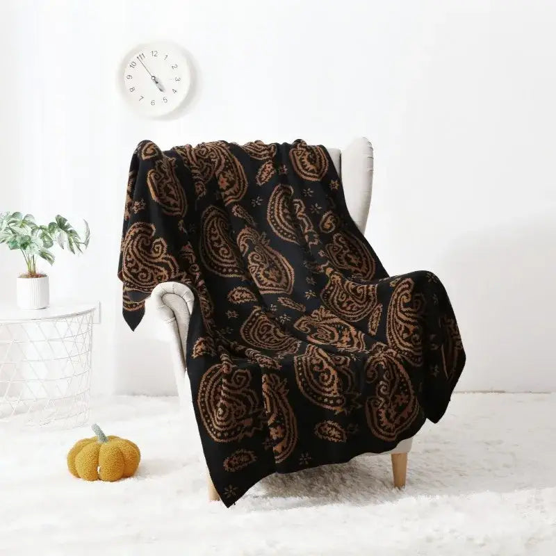 Black throw blanket with intricate gold decorbites cashew pattern draped over white armchair for living room decor
