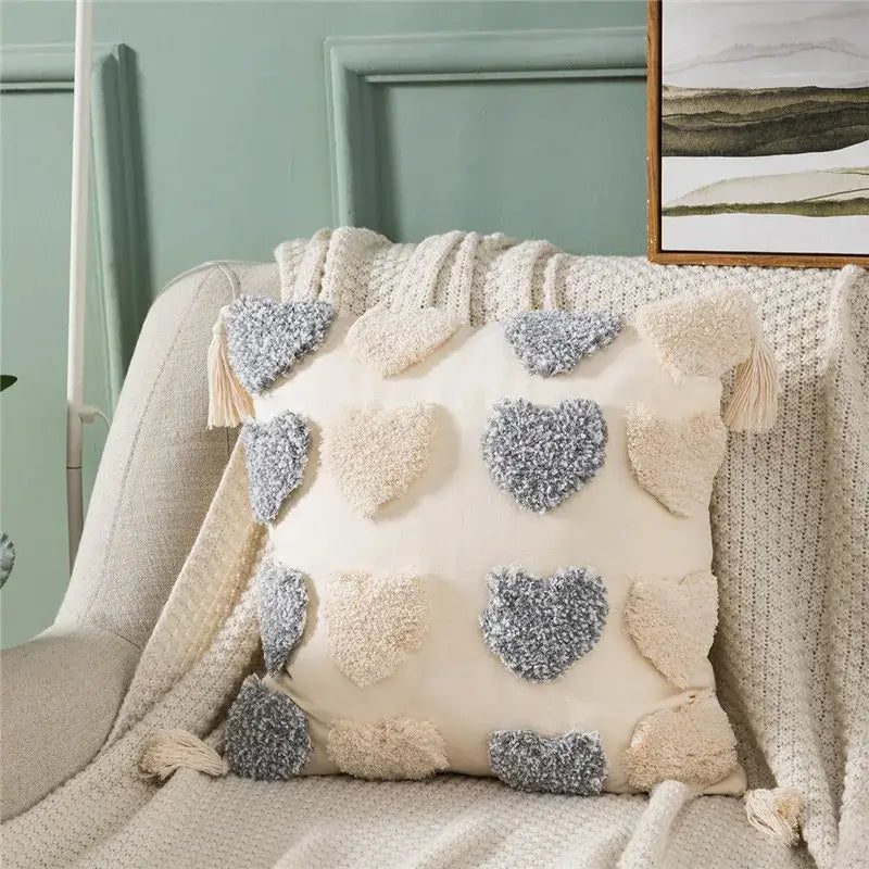 Cream-colored cushion cover featuring decorbites heart embroidery with orange and grey textured appliqués and tassels