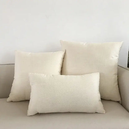 Three off-white linen throw pillows of varying sizes with orange textured cushion cover on a decorbites ivory sofa cushion