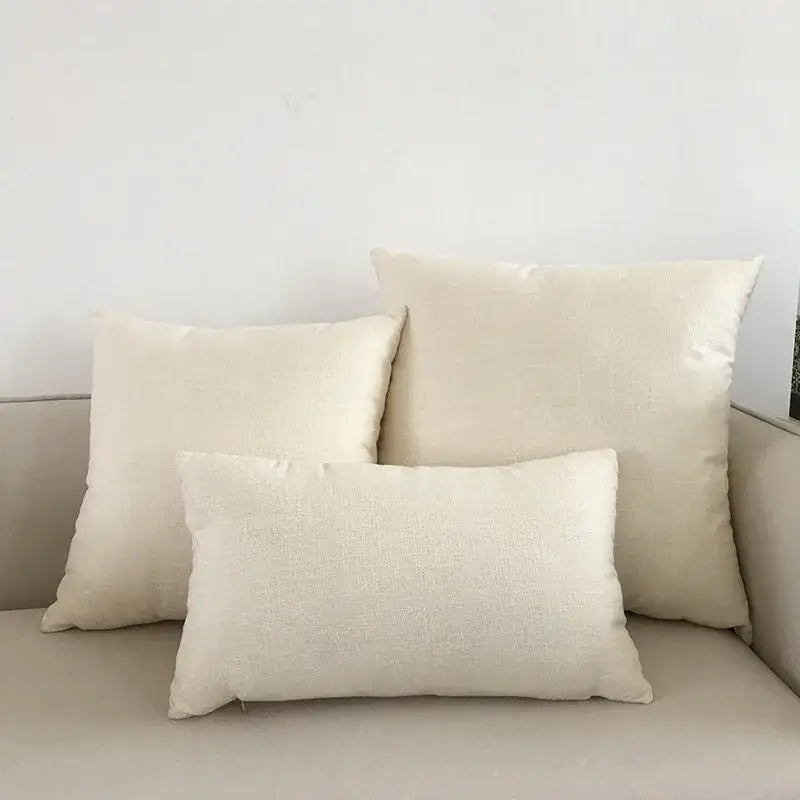 Three off-white linen throw pillows of varying sizes with orange textured cushion cover on a decorbites ivory sofa cushion