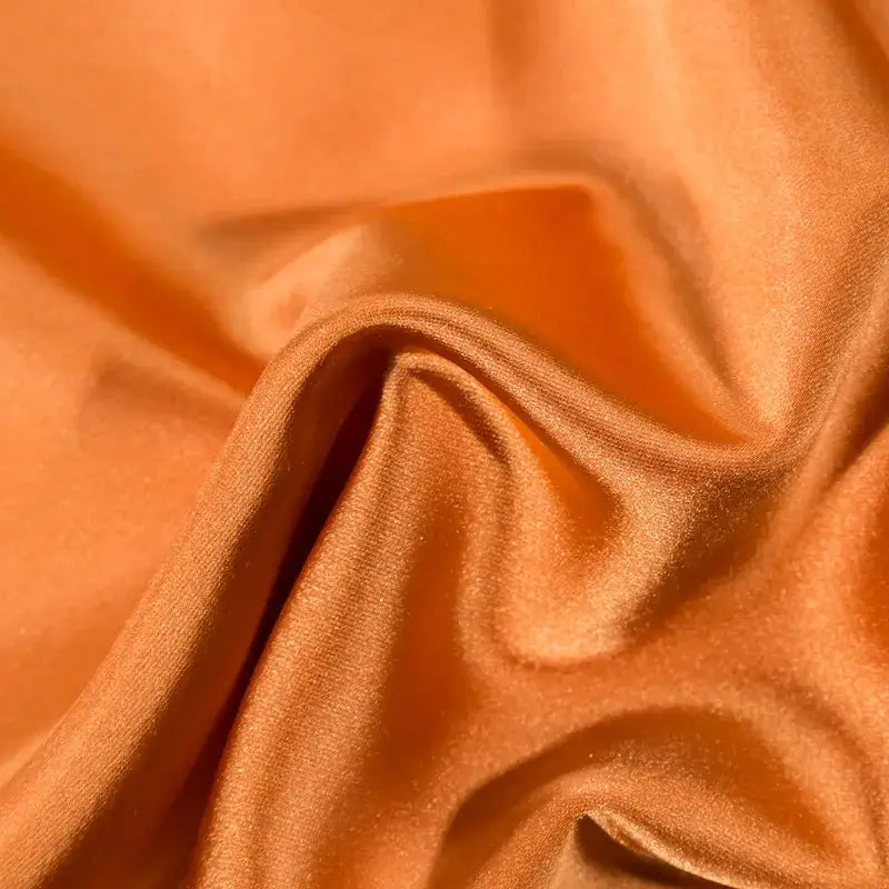 Smooth satin-like orange fabric with subtle sheen and folds in orchid and blue floral 200s embroidery egyptian cotton bedding set