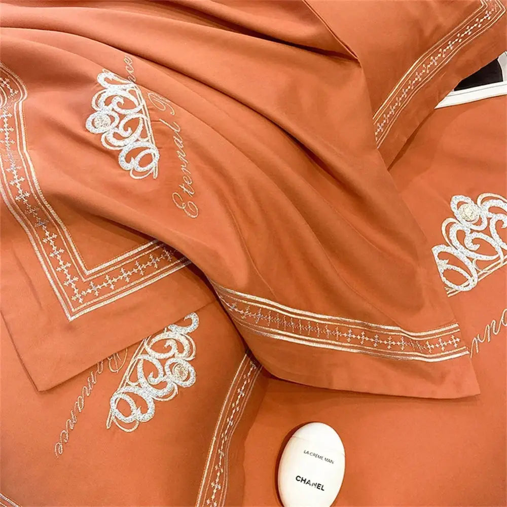 Coral-colored satin pillowcases with white embroidered floral and script designs from orchid satin 1200tc egyptian cotton bedding set