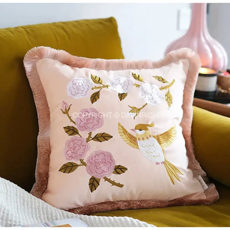 A soft peach-colored pillow cover with delicate pink and white bamboo embroidered floral design and fringed border for decorbites
