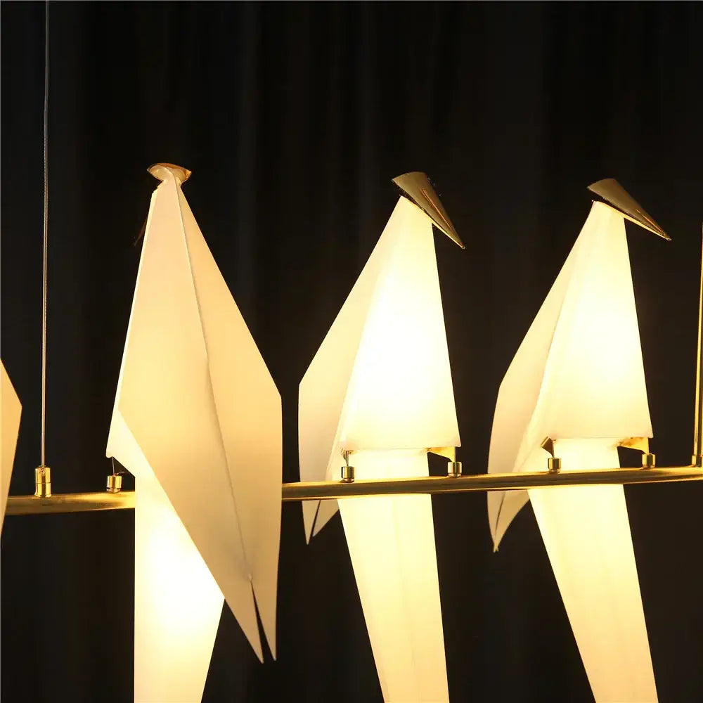 Three illuminated origami crane bird design led pendant lights with white paper bodies and gold metal beaks by decorbites