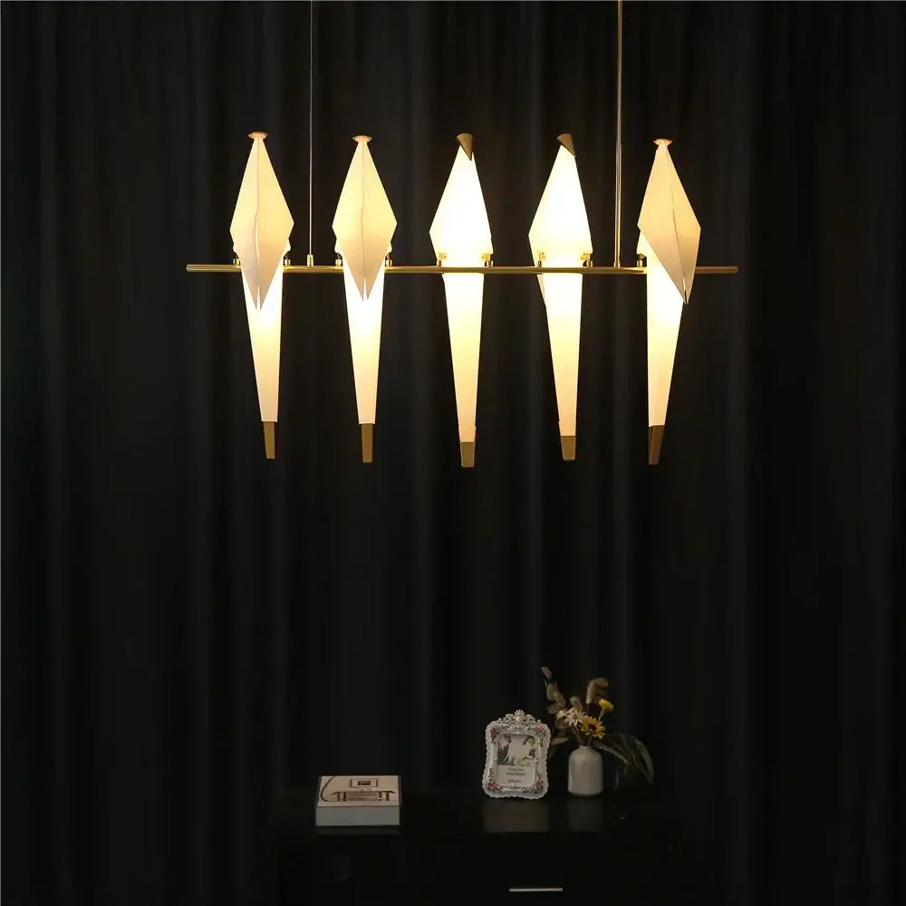 Five illuminated white gold origami crane bird design led pendant lights with warm glow suspended from brass rods for dining room decorbites bird design