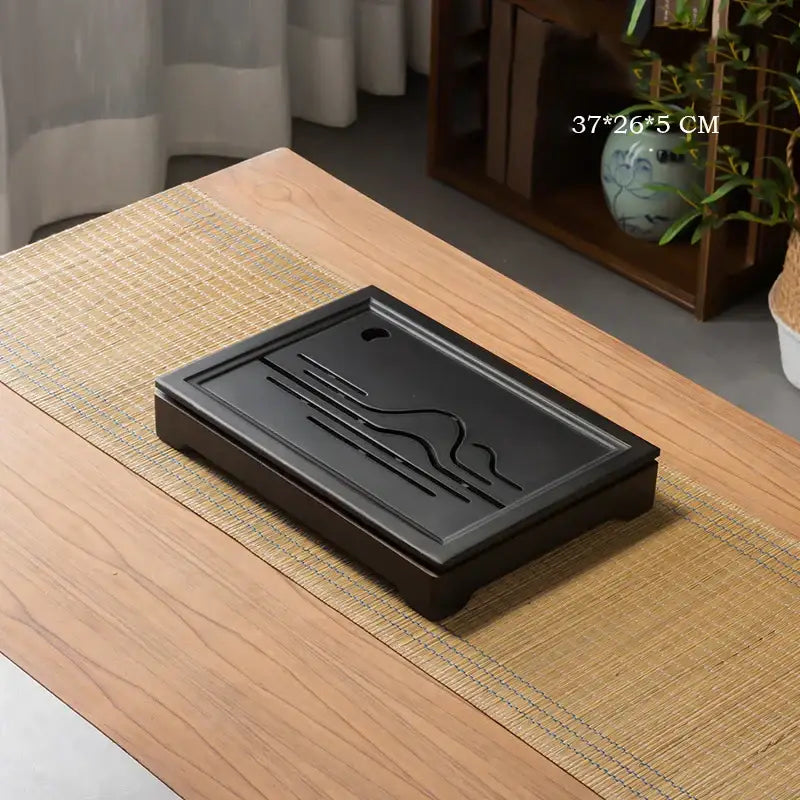 Ornate black bamboo tea tray with engraved wave patterns and drainage hole crafted from polished stone for dining room use