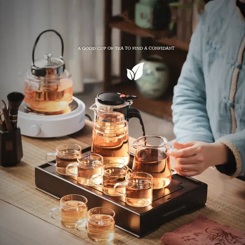 Clear glass teapot with black lid and handle on an ornate black bamboo tea tray with drainage for dining room use