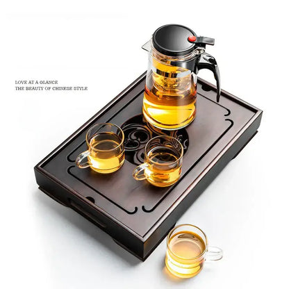 Clear glass teapot with black lid on an ornate black bamboo tea tray designed for dining room water storage drainage