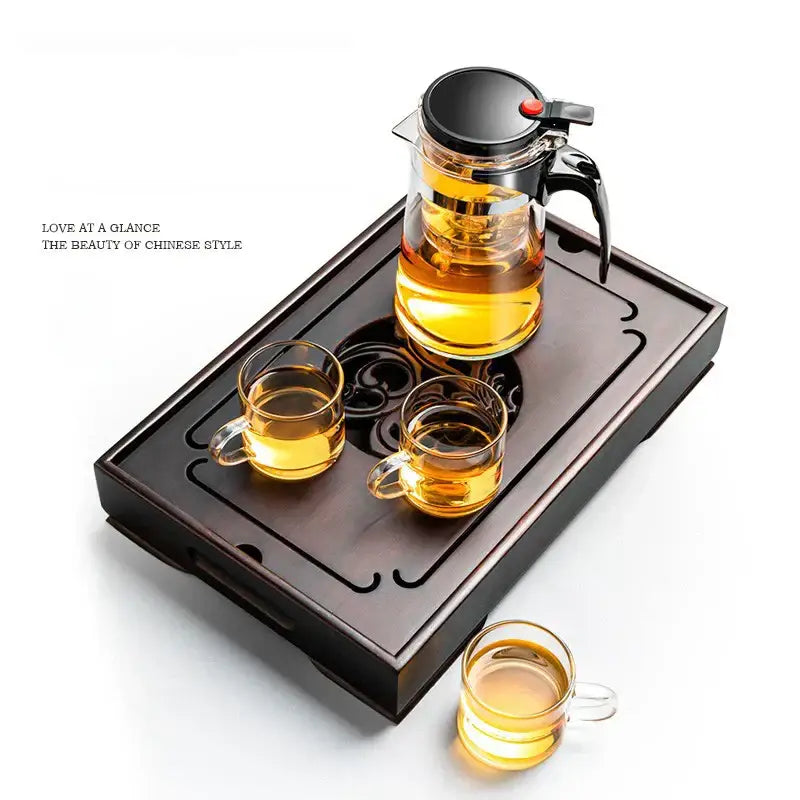 Clear glass teapot with black lid on an ornate black bamboo tea tray designed for dining room water storage drainage