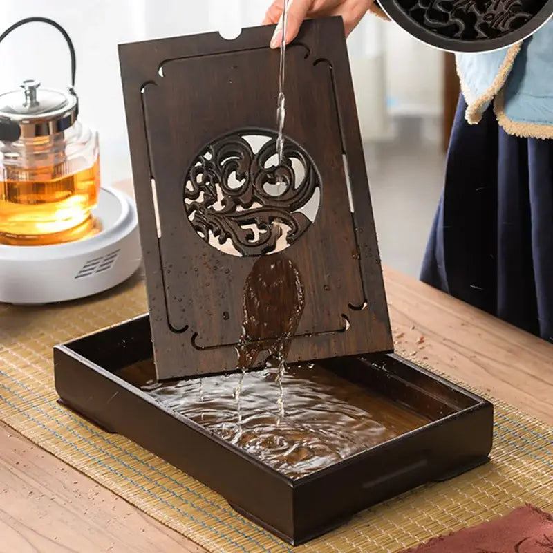 Ornate black bamboo tea tray featuring dark wood with intricate circular carvings and waterfall drainage design
