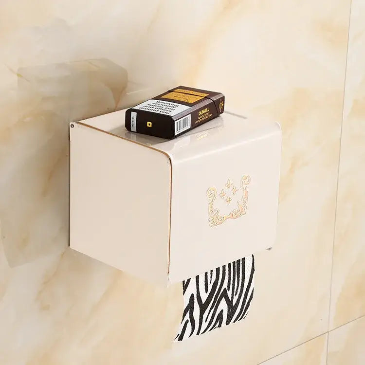 Cream-colored wall-mounted toilet paper box with gold design holding black carved aluminum decorbites black carved roll