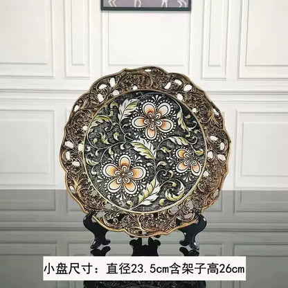 An ornate circular decorative plate with black center and gold border complementing resin vase dried flowers decor