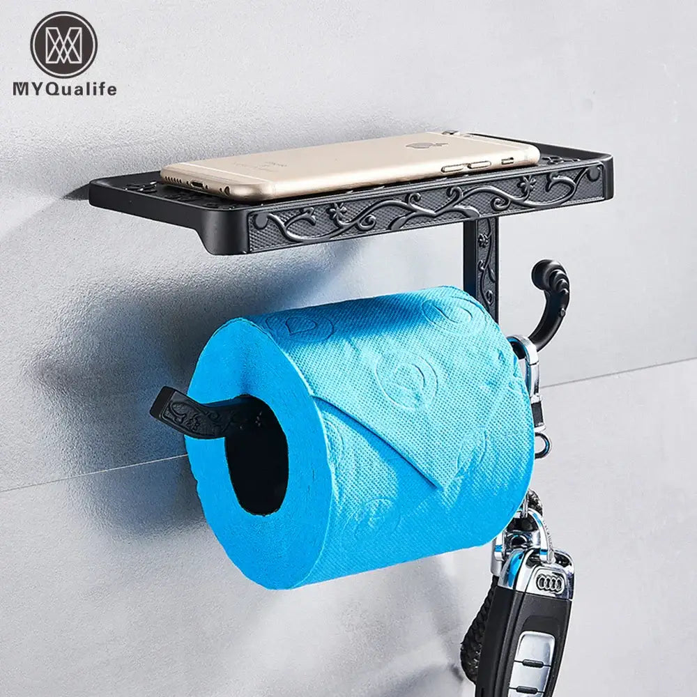 Ornate black metal toilet paper holder with integrated phone shelf and key hook holding a gold smartphone