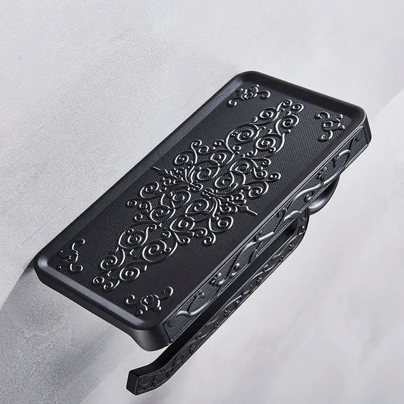 Ornate black metal toilet paper holder with phone shelf featuring intricate silver embossed floral design and integrated clip