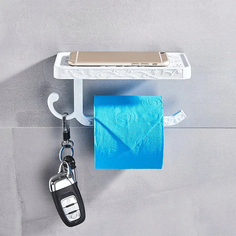 White ornate metal toilet paper holder with phone shelf featuring bright blue tissue and gold smartphone resting on it
