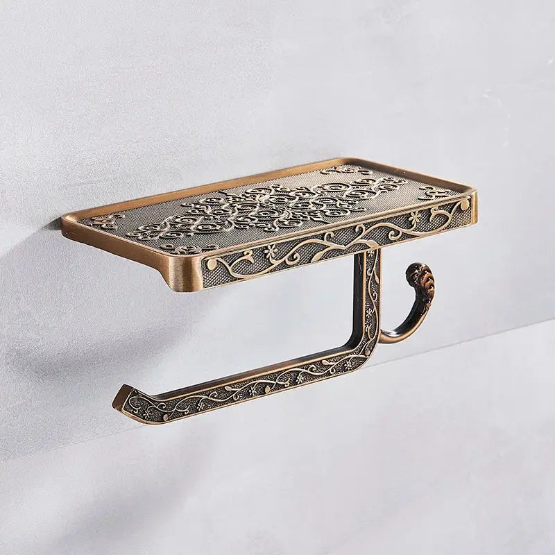 Antique brass toilet paper holder with ornate floral scrollwork and rectangular shelf for bathroom storage and phone
