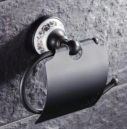 Black matte metal toilet paper holder with ornate white ceramic plate featuring black floral detailing in bathroom accessories set