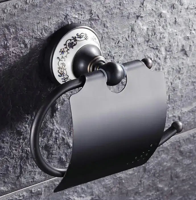 Black matte metal toilet paper holder with ornate white ceramic plate featuring black floral detailing in bathroom accessories set